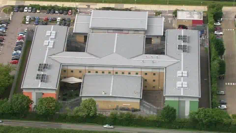 Brook House detention centre seen from the air. It is in a cross shape, and can be observed to be laid out in a wing type structure.
